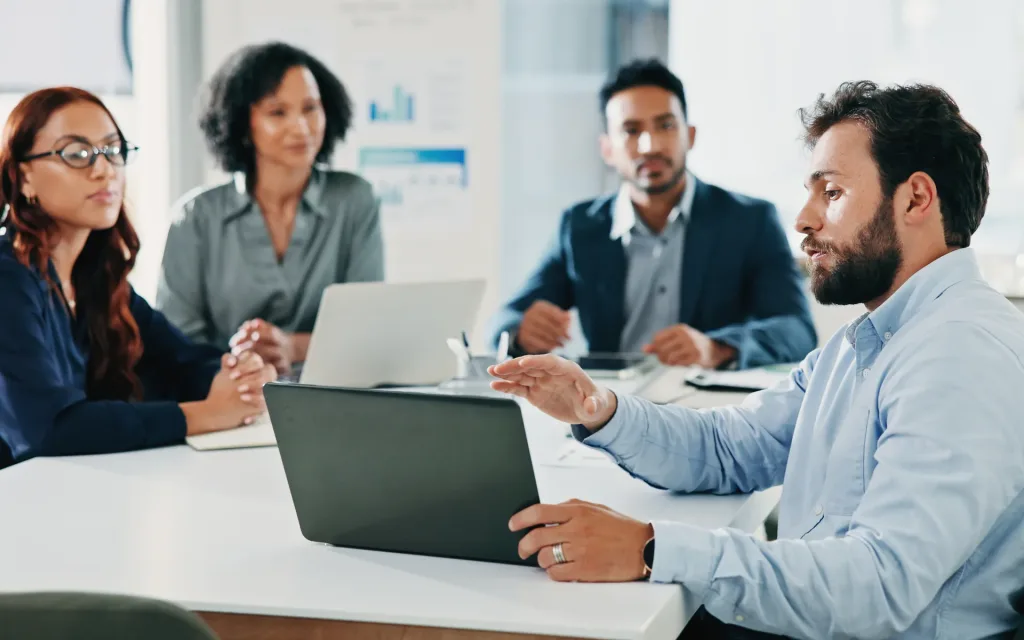A government finance team in a boardroom reviewing labor cost proposals and budget data on a laptop