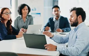 A government finance team in a boardroom reviewing labor cost proposals and budget data on a laptop